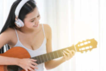Fototapeta premium Blur Attractive girl wearing white headphones. Beautiful woman playing guitar in the morning, ray light