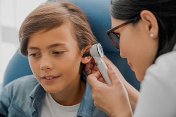 Female doctor examining boy's ear with otoscope