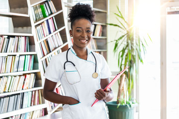 Doctor with a stethoscope, holding a notebook in her hands. African female doctor filling up...