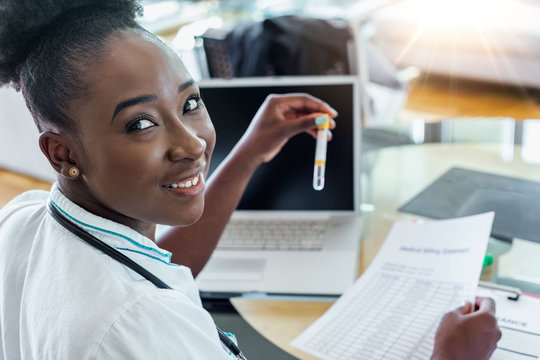 Female doctor in white coat holding blood test tubes in hands while wrapped up in work at modern lab. Female life science professional holding glass cuvette. Healthcare and biotechnology concept.