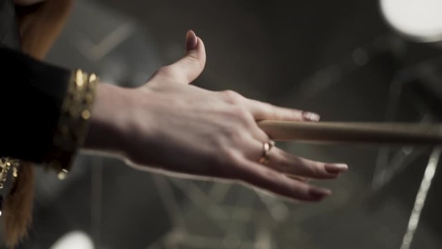 Close up of woman drummer hands holding drumstick on dark rehearsal room background. Action. Female musician hand holding and spinning wooden drumstick.