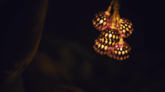 Magic hot light from lanterns falls on the woman eyes. The naked adult sexy caucasian girl lies at night on the bed and holds warm lamps in her hands. Christmas toy in black background. Indoor.