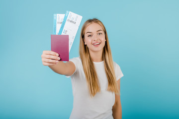 beautiful young smiling blonde girl with passport and airplane tickets isolated over blue