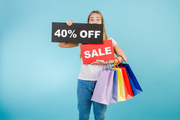 surprised young woman with 40% off sale sign and colorful shopping bags isolated over blue