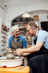 Senior woman spinning clay on a wheel with teacher at pottery class