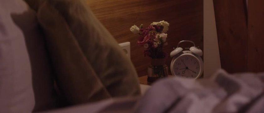 A vintage alarm clock on a nightstand next to an unmade bed - Ein retro Wecker auf einem Nachttisch neben einem ungemachten Bett