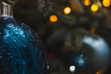soft focus water drops on Christmas tree toy blue ball surface with blurred garland yellow illumination background