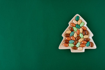 Candy in christmas tree shaped plate on green background .  Top view with copy space