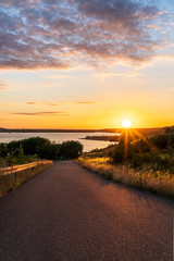 Fototapeta premium Asphalt road leading to a lake during a beautiful summer sunset 