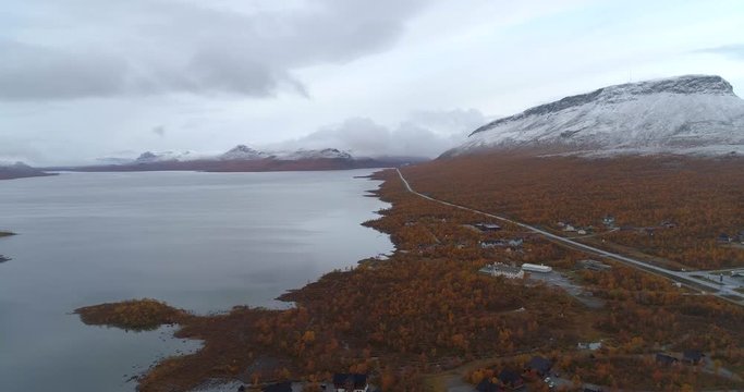Kilpisjarvi lake, Aerial, tracking, drone shot, overlooking the e8 road the town and first snow on Saana tunturi fell, on a cold, autumn morning, in Enontekio, Finland