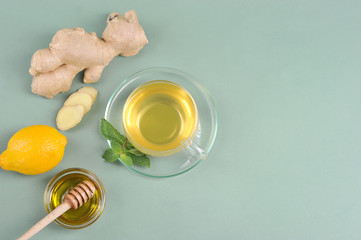 Drink with ginger and honey on a light surface.  Next to the cup are the ingredients for making the drink: ginger, mint, honey and lemon.  Free space for text.  View from above.  