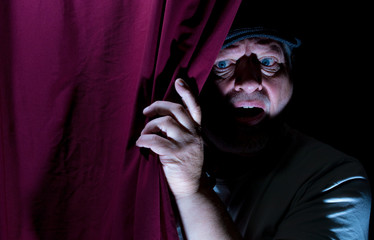 An elderly man with hat is standing in a room behind a curtain. He looks scared. Concept: facial...