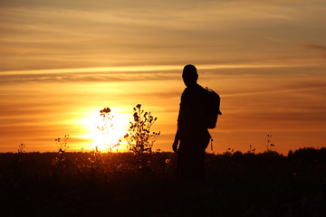 Silhouette of a traveler with a backpack on a sunset background..A tourist is watching the sunset.