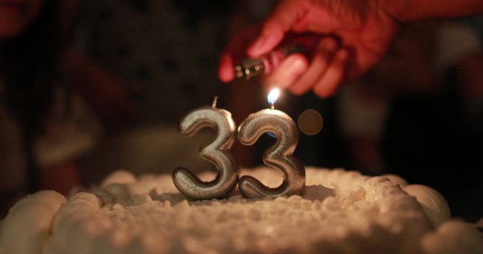 Closeup of hand lighting birthday cake candle with lighter celebrating 33 years of age
