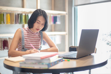 Young Asian woman using laptop computer and tablet PC to working in the modern co working space