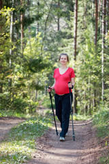 Pregnant woman walking in a summer forest using hiking poles