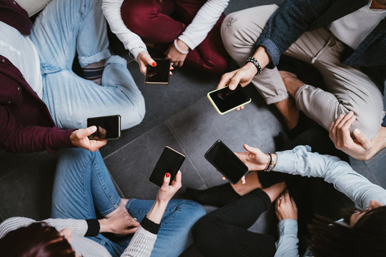 Young people in a circle use the smartphone together - Millennials to sit on the ground with their cell phones