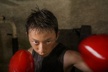 tough and cool young boy punching on heavy bag . 13 or 14 years old Asian teenager training Thai...