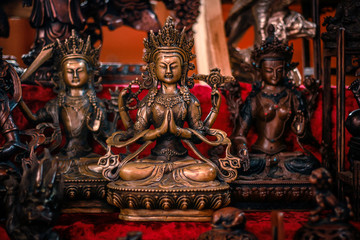 Buddhist figurines and masks of mythological characters in gold and bronze on a burgundy with a red background - obrazy, fototapety, plakaty