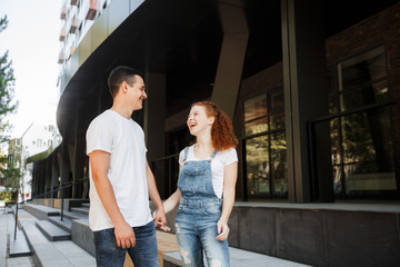 A young couple is walking in the modern city, holding hands. Inspect the conceptual archeology.