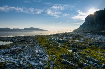 Naklejka premium Golden morning as the sun rises above the rocks reflecting over the low tide, St-Lawrence river shore, Quebec, Canada