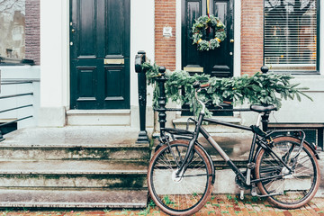 Fototapeta na wymiar Cozy city picture, a bicycle parked at the entrance to the house decorated with Christmas tree branches.