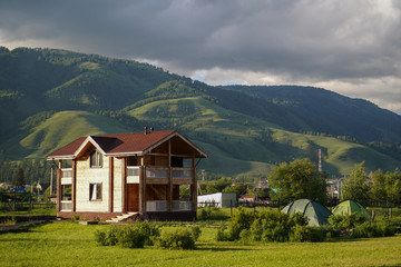 Fototapeta na wymiar Green meadow with touristic cottage and touristic tents, and growed mountains