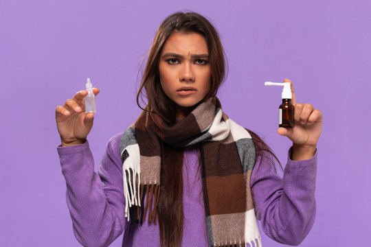 Pretty african-american girl in a sweater and cosy checked scarf hold medical drug to cure common cold standing isolated over purple background. Catching cold in winter.