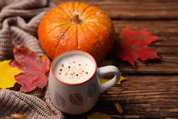 Pumpkin spiced latte or coffee in glass decorated knitted scarf on turquoise vintage background. Autumn, fall or winter hot drink. Cozy breakfast.