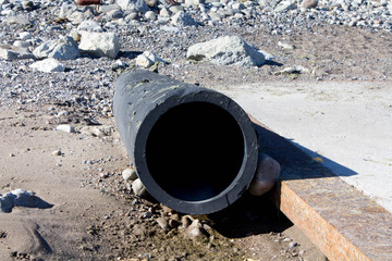 heavy black drain pipe onto a sandy beach without water