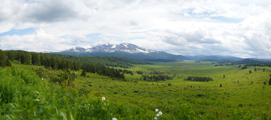 Mountain valley view with green grass field, cloudly sky and mountains