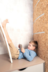A little boy is playing the tablet in various poses alone at his room