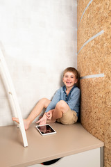 A little boy is playing the tablet in various poses alone at his room