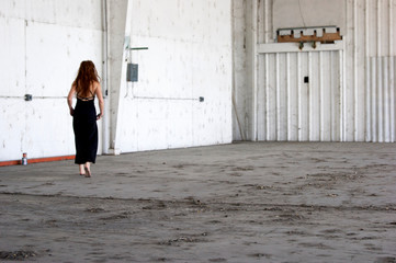 A woman with long red hair and fancy party dress is walking barefoot at old industrial loading dock, soft focus. - Powered by Adobe
