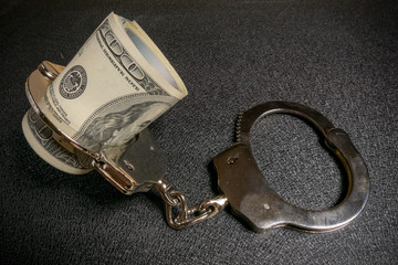 Roll of american hundred dollar bills in handcuffs on black background. Corruption, robbery and fraud concept