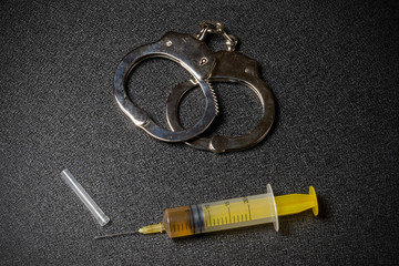 Handcuffs and a syringe with a dose of the drug on a black background