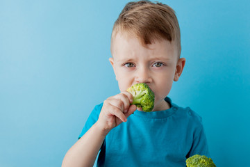 Little kid holding broccoli in his hands on blue background. Vegan and healthy concept