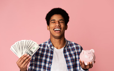 Black guy holding money and piggybank on pink background