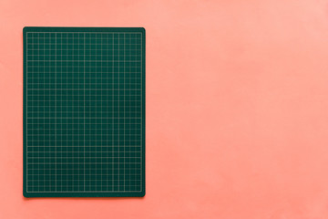 Top view of green rubber cutting mat on the left side over pink color paper background. Background...