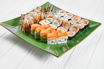 Close up view on set of assorted roll and sushi on green plate isolated on white wooden background. Sushi with salmon, eel. japanese sushi food