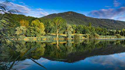 Fototapeta premium View of the lake, forest, mountains and blue sky with clouds.Lake Machilly, Le Signal des Voirons mountain peak,Haute-Savoie in France.