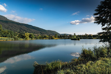 Landscape of lake, mountains, vegetation, village and blue sky with white clouds.Lake Machilly, Haute-Savoie in France.