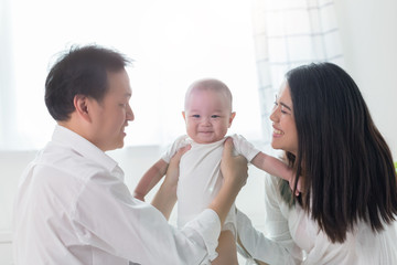 Young happy Asian mom dad and newborn baby infant boy playing at home.