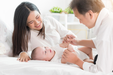 Young happy Asian mom dad and newborn baby playing at home.
