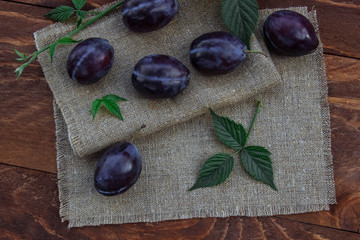 Ripe, juicy sweet blue plums on the brown wooden table and linen tablecloth in the kitchen with green leaves to decorate the view from the top