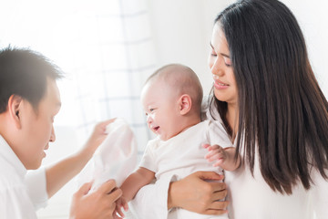 Young happy Asian mom dad and newborn baby playing at home.