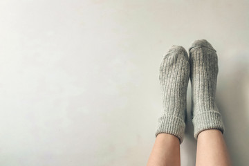 Women wearing grey knitted cozy socks on gray background. Сopyspace for text 