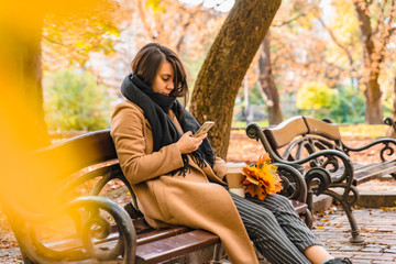 Fototapeta na wymiar woman sitting in city park drinking coffee taking picture of bouquet of maple leaves