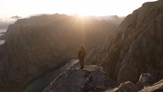 Midnight sun in Lofoten, Norway. Man standing on an epic rock.