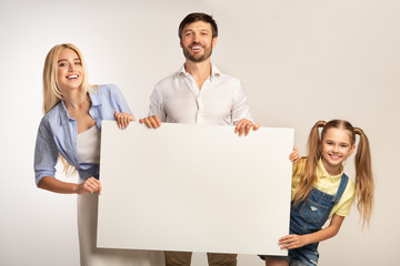 Parents And Daughter Holding White Board Smiling At Camera, Studio